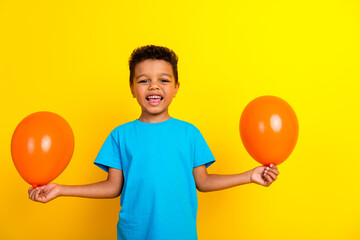 Photo of mixed race little child with curly hair dressed blue stylish t-shirt holding two bubbles isolated on vibrant yellow background