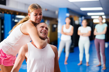 Determined young girl performing rear choke hold while sparring with male opponent during self...