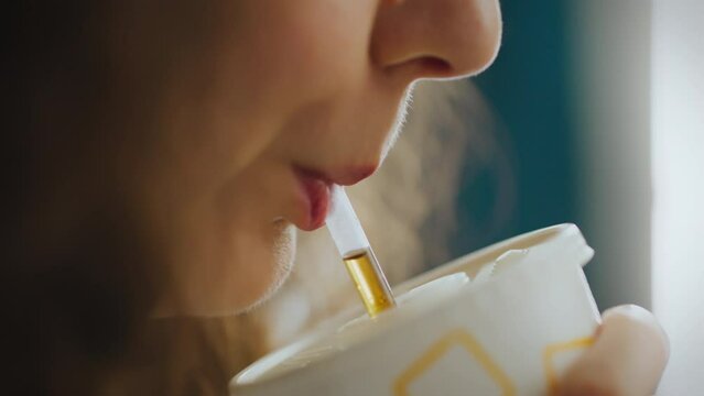 Beautiful girl in a fast food street eatery drinking a chilled cola soda drink with ice using a straw. Close-up of a girl's face drinking cola through a straw while sitting in a fast food restaurant