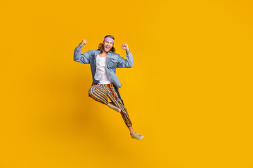 Fototapeta na wymiar Full body portrait of cool young man raise fists yes jump wear denim shirt isolated on yellow color background