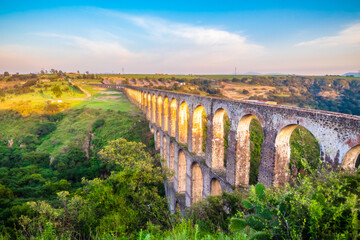 Fototapeta na wymiar Aqueduct between mountains at sunset with cloudy sky in arcos del sitio in tepotzotlan state of mexico