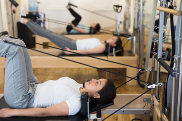 Side view of focused sportswoman stretching body on pilates chair while doing forward bends during...