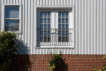 Fototapeta na wymiar White Window on Corrugated Metal Siding Over Brick Foundation, Closed Metal Balcony