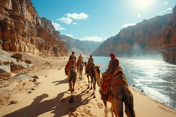 Selbstklebende Fototapeten Group riding camels by river in picturesque landscape with mountains and sky © Vladimir