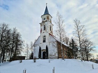 Fototapeta na wymiar An old small church on snow-covered hill in the Latvian village of Remte in December 2021