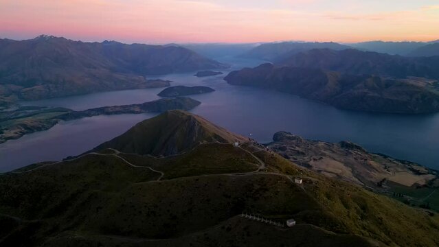 Aerial orbit of tourists on Roy's Peak viewpoint overlooking lake Wanaka during pink sunrise