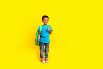 Fototapeta na wymiar Full body photo of adorable small child dressed blue t-shirt jeans hold bag showing thumb up isolated on vibrant yellow background