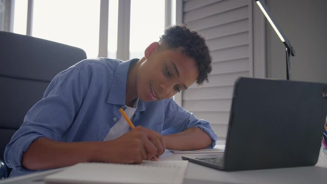 Teenage boy sitting at desk in bedroom at home doing homework on laptop - shot in slow motion