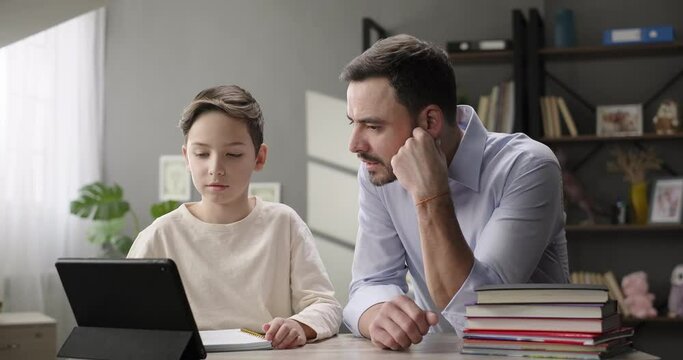 Happy family father and son doing homework together at home desk. Father helping son, study online with digital tablet. Children private education