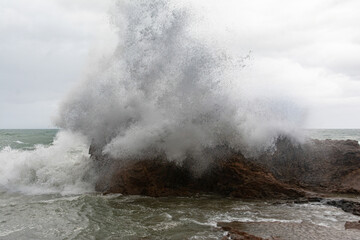 Fototapeta na wymiar Immense waves hitting a large rock at the edge of the beach. Force of nature.