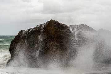 Immense sea rock covered by a large wave. Force of nature.
