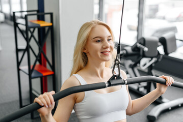 Fototapeta premium young athletic caucasian woman trains in fitness gym, doing thrust of upper block to chest, blond girl in white top and black leggings, healthy lifestyle concept