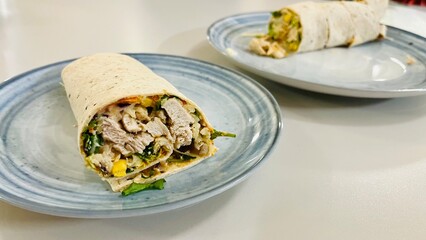 A lavash roll with fried pieces of chicken breast meat with vegetables, corn lies on a gray plate on a white table. Healthy snack. healthy eating. low calorie diet. two plates with lavash roll