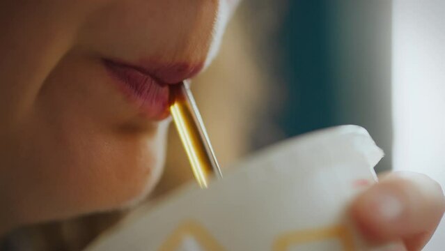 In a fast food street eatery, a young beautiful girl drinks a chilled cola through a straw while sitting at a table and enjoying the atmosphere of the surrounding city noise. Slowly enjoying the drink