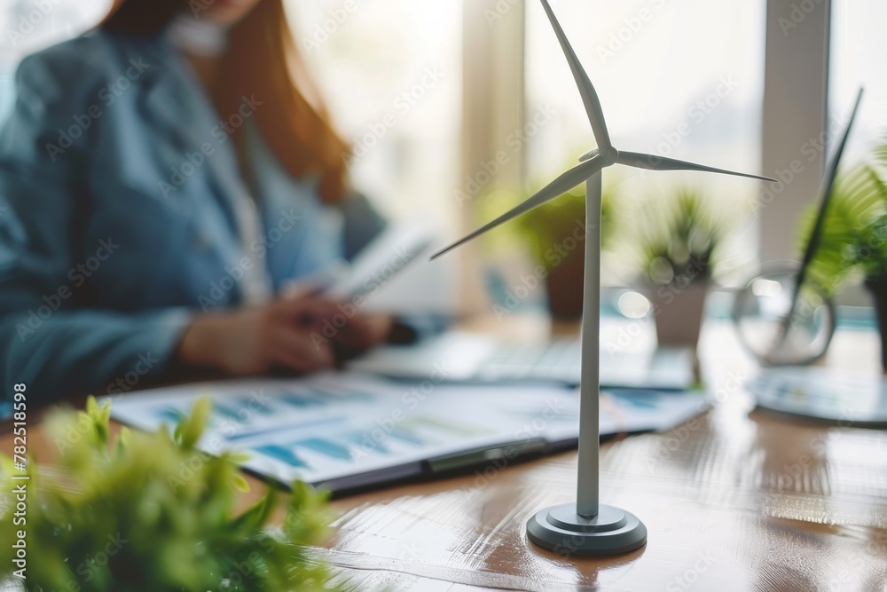 Poster an office setting with a person analyzing reports next to a miniature wind turbine model, representi