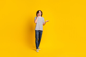Fototapeta na wymiar Full size portrait of nice young man walk speak phone wear striped t-shirt isolated on yellow color background