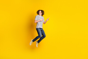 Fototapeta na wymiar Full size portrait of nice young man jump point fingers empty space wear striped t-shirt isolated on yellow color background