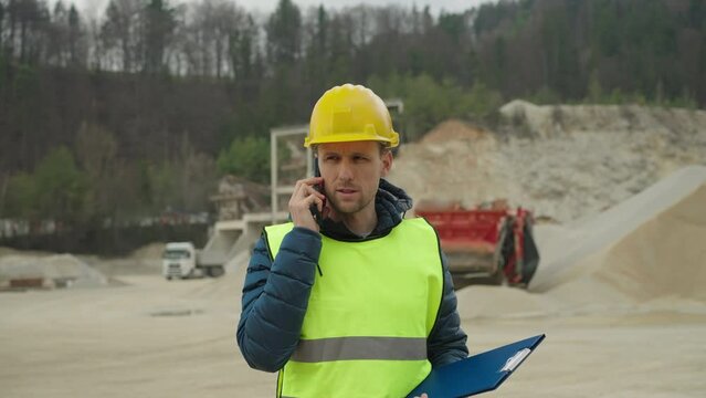 Waist up shot - Quarry worker wearing reflective vest and a helmet talking to the supervisor on the phone