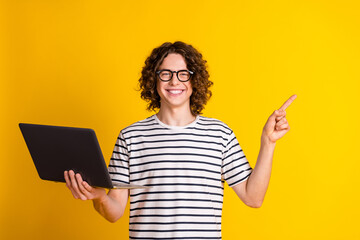 Photo of nice young man hold laptop direct finger empty space wear striped t-shirt isolated on yellow color background