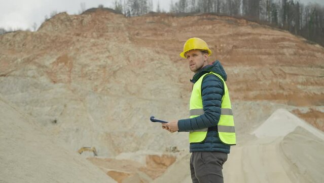 Waist up shot - Inspector in reflective vest and protective helmet looking at documents while on site.