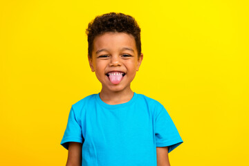 Photo of funky positive funny child with curly hair dressed blue t-shirt showing tongue fooling...