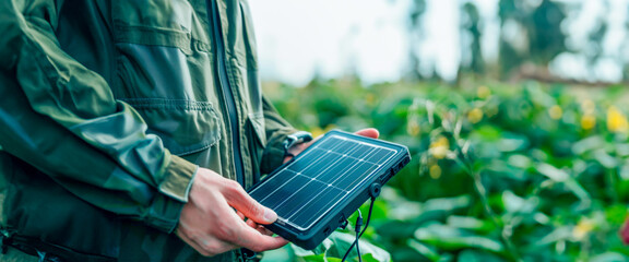 Hands adjusting a compact solar charger outdoors, representing the trend of personal renewable energy sources. Environmental Protection. Heating and irrigation system. Banner. Copy space