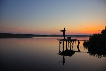 Amazing sunset over calm lake with fisherman catching fish.