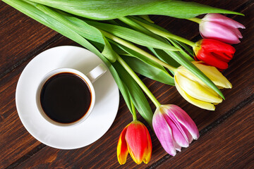 A cup of coffee, a bouquet of tulips on a dark wooden table.
