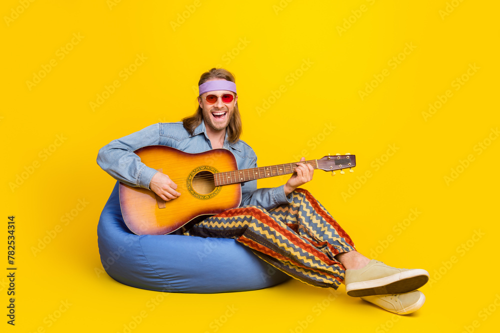 Sticker Full body portrait of cool young man sit bag play guitar wear denim shirt isolated on yellow color background