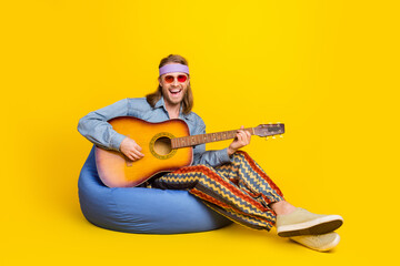 Full body portrait of cool young man sit bag play guitar wear denim shirt isolated on yellow color background