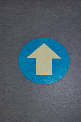 Light blue colored arrow pointing up on the floor of a walkway