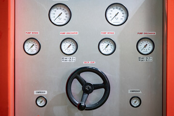 A collection of gauges resembling those found on a firetruck, with a prominent central display, stands out against a shiny chrome surface.
