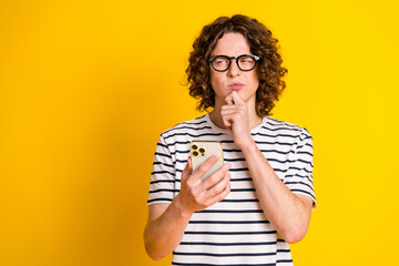 Photo portrait of pretty teen male touch chin hold device thoughtful wear trendy striped outfit isolated on yellow color background