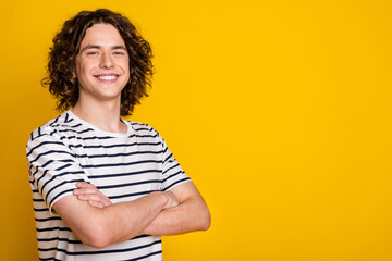 Photo of nice young man beaming smile crossed arms empty space wear striped t-shirt isolated on yellow color background