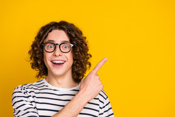 Photo of young amazed teenage guy in striped t shirt direct finger billboard sale presentation isolated on yellow color background
