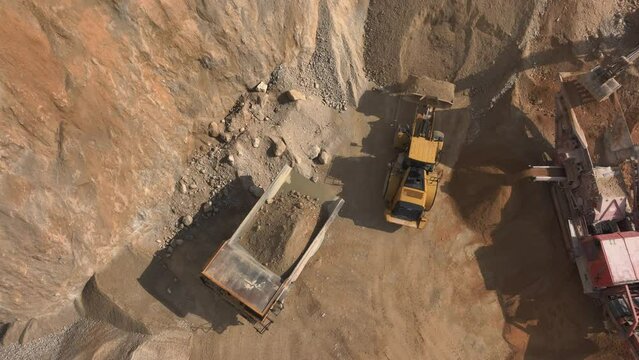Aerial shot - Excavator loading up gravel from a pile and on to a dump truck. Work happening on ht quarry grounds.
