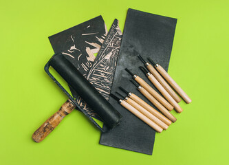 Linocut tools. Cutters, roller, black linoleum on a green background. Handicraft and design...