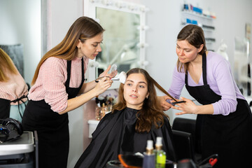Two young women working in a beauty salon as a make-up artist and a hairdresser serve a young...