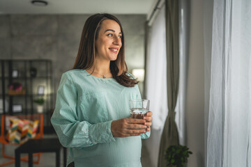 Adult pregnant women sit and hold glass of water at home