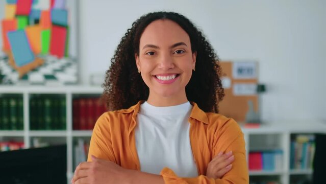 Video of a gorgeous positive confident brazilian or hispanic curly haired young woman in a casual stylish clothes, stand in the office near workdesk with arms crossed, looks at camera, smiling happily