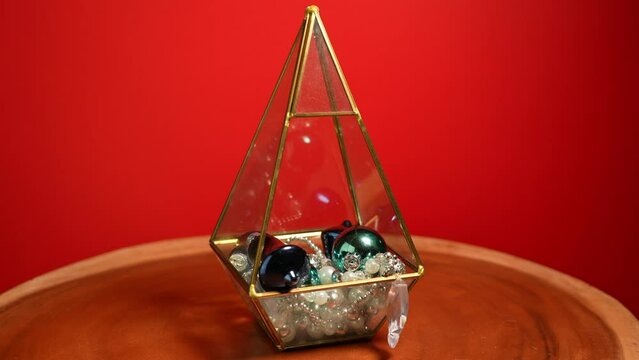Christmas golden terrarium decoration with holiday balls and jewellery. Rotation on red background. Home celebration setup. New Years and Christmas Eve.