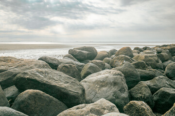 Stone boulders on the beach at low tide.Wadden Sea Coast.Stone groyne on cloudy sky background.. Marine photo wallpaper.Nature of the North Sea coast. Frisian Islands of Germany.  - 782568528