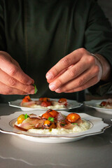 Chef hands adding basil leaves to stracciatella di bufala with roasted tomatoes and bacon