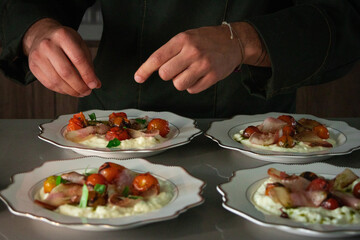 Chef hands adding basil leaves to Stracciatella di bufala with roasted tomatoes and bacon