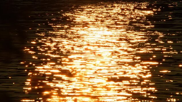 Reflection of sunlight like fire, sun set and golden hour over lake surface in slow motion.