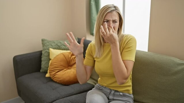 Young, attractive blonde woman dons t-shirt indoors, grimacing as disgusting, intolerable stench invades her home. nose pinched, holding breath to block smelly stink. disgust visible.