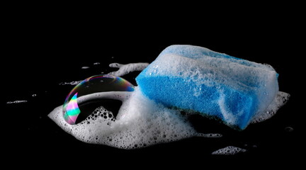 Soap foam with bubbles and blue sponge isolated on black