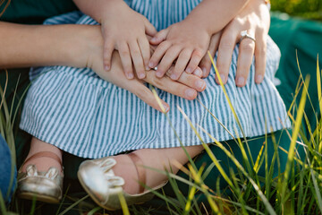 Close-up of a child&rsquo;s and an adult&rsquo;s hands together, resting on a striped dress, surrounded by grass