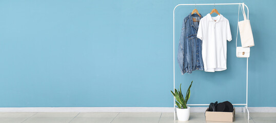 Rack with stylish clothes, accessories and houseplant near color wall