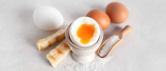 Holder with soft boiled egg, toasted bread and scoop on white table